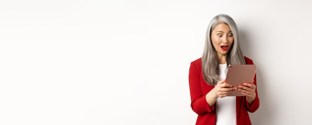 Free photo business asian senior woman staring at digital tablet screen with amazed and surprised face reading