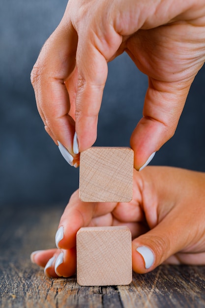 Business concept on dark and wooden background side view. hands arranging wooden cube as stack.