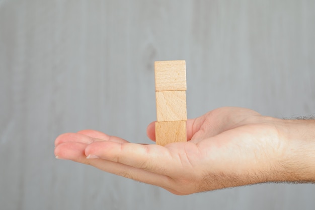 Business concept on grey table side view. hand holding tower of wooden cubes.