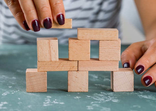 Business concept side view. woman building up tower from wooden blocks.