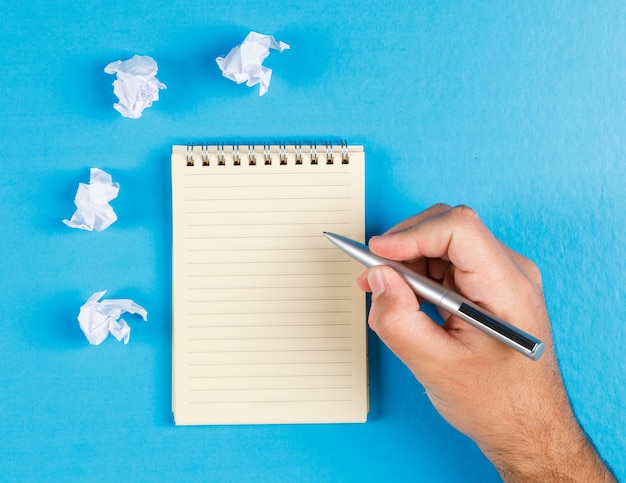 Free photo business concept with crumpled paper wads on blue background flat lay. businessman taking notes on paper.