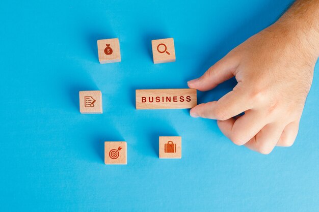 Business concept with icons on wooden cubes on blue table flat lay. hand holding wooden block.