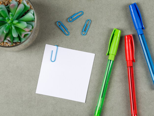 Business concept with pens, paper clips, sticky note, plant on grey surface flat lay.