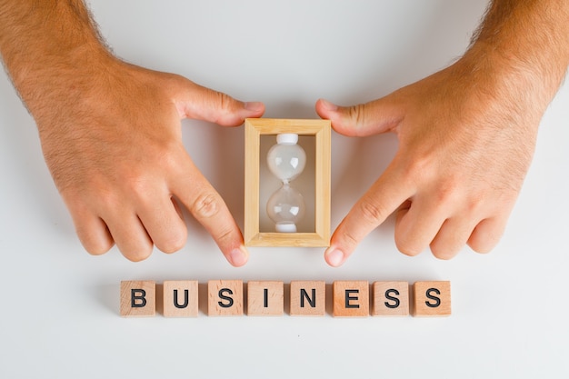 Business concept with wooden blocks on white table flat lay. man hands holding hourglass.