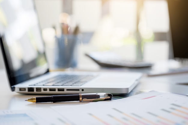 Business desk with a keyboard, report graph chart, pen and tablet on white table