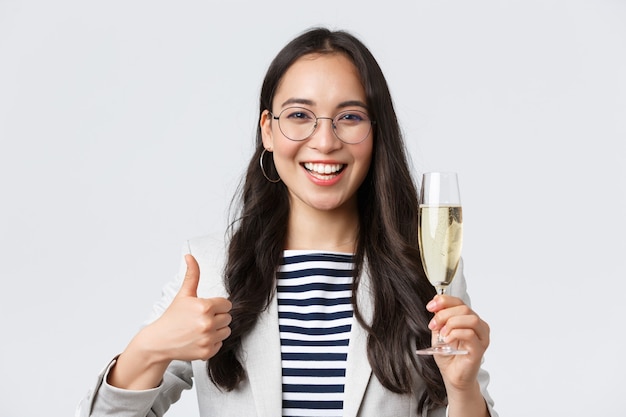 Business, finance and employment, female successful entrepreneurs concept. Happy asian businesswoman celebrating, having office party, drinking champagne and show thumbs-up