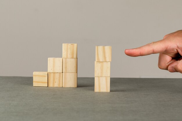 Business growth concept on grey and white wall side view. man showing wooden blocks tower.