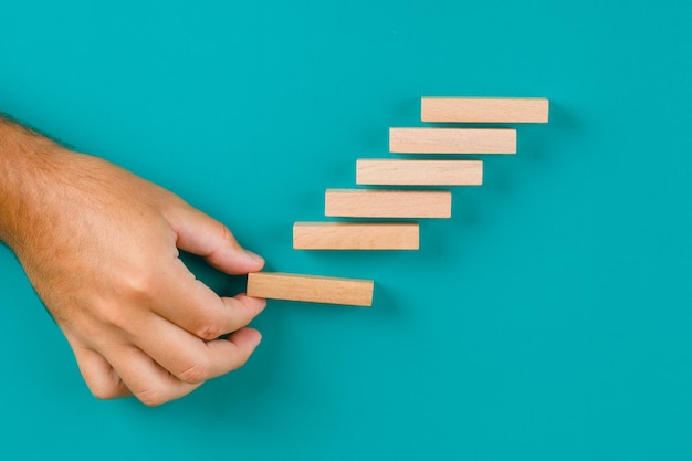 Free Photo business growth concept on turquoise table flat lay. hand stacking wooden blocks.