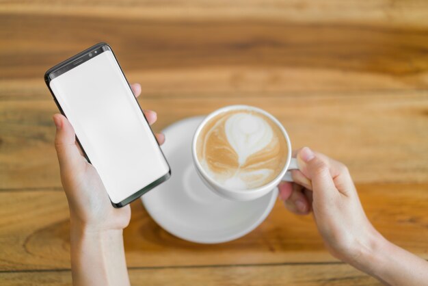 Business hand with mobile phone and latte art coffee .