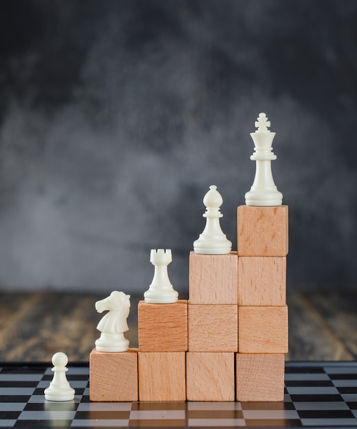 Free photo business hierarchy concept with chessboard, figures, pyramid of wooden blocks on foggy and wooden table side view.