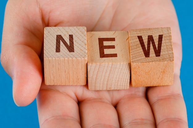 Free photo business idea concept on blue table close-up. hand holding wooden cubes with word new.