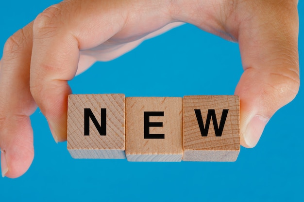 Free Photo business idea concept on blue table side view. hand holding wooden cubes with word new.