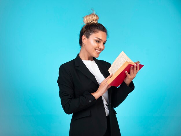 Business lady in black blazer with a red book and reading it.