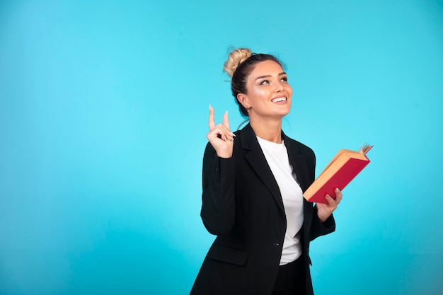 Business lady in black blazer with a red book thinking. 