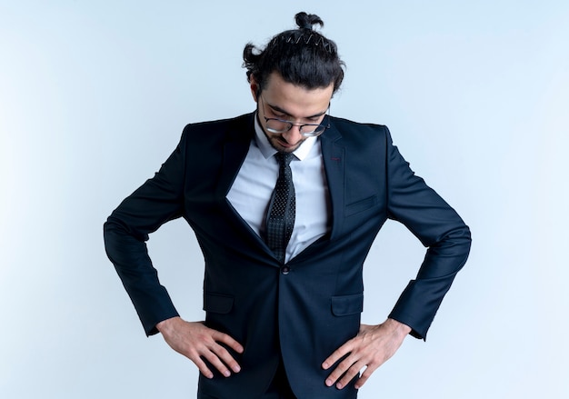 Free Photo business man in black suit and glasses looking down with arms at hip tired and bored standing over white wall