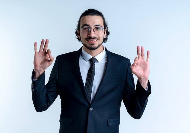 Free photo business man in black suit and glasses looking to the front showing ok sign with both hands smiling standing over white wall