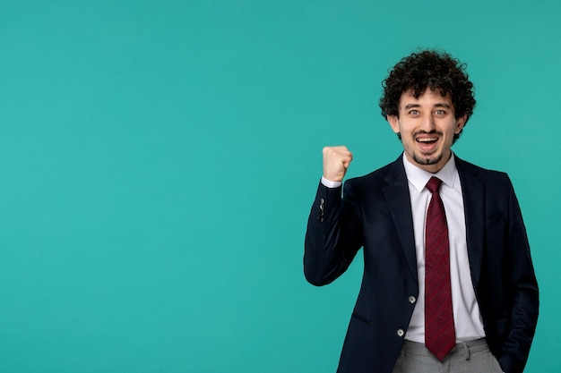 Business man curly cute handsome guy in black suit and red tie excitingly holding fist up