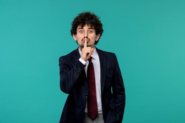 Business man curly cute handsome guy in black suit showing silence gesture sign