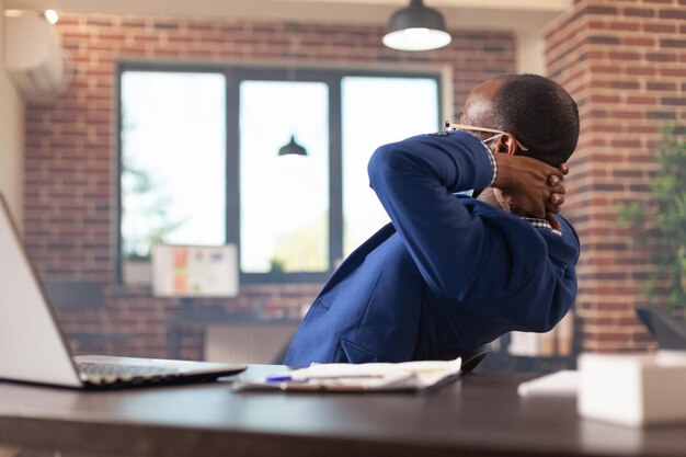 Business man finishing work and relaxing on break in office during coronavirus pandemic. Satisfied employee wearing face mask, sitting with hands over head to relax after getting job done.