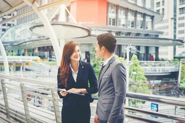 Business man pointing at document with smile and discussing something with her coworker while standing in front of office.