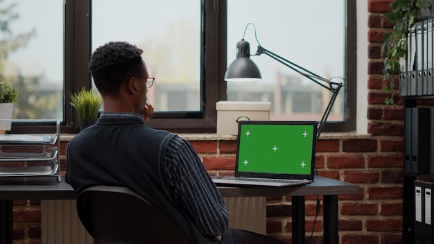 Business man working with laptop and green screen on display, using chroma key template with mock up background and isolated copy space. Company employee with blank screen in office.