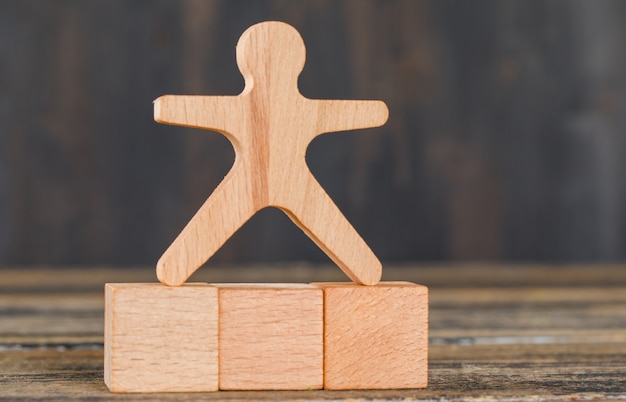 Free photo business success concept with human model on wooden cubes on wooden table side view.