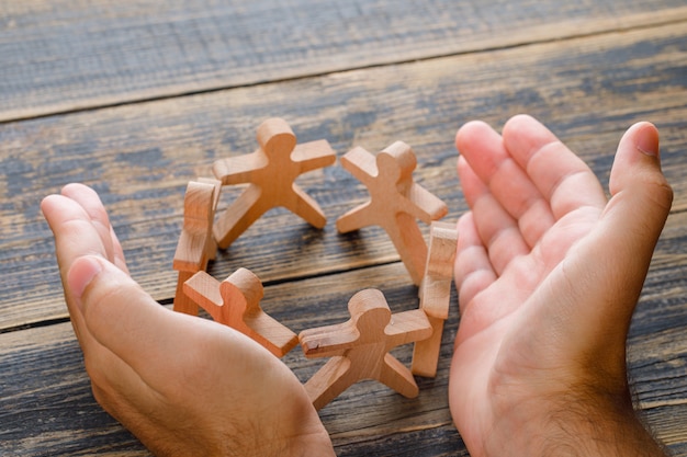 Free photo business success concept on wooden table top view. hands protecting wooden figures of people.