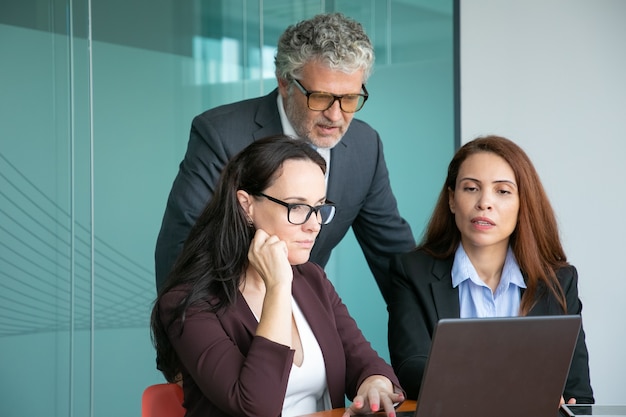 Business team of three watching presentation on computer, looking at display, discussing details