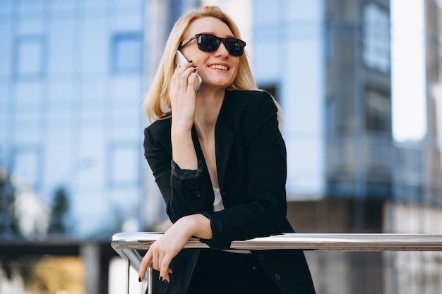 Business woman by the skyscraper using phone