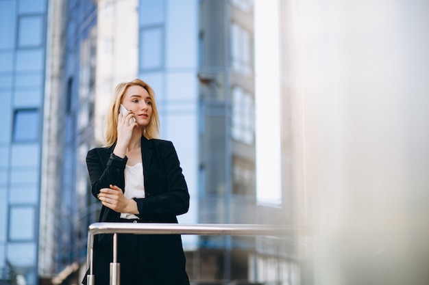 Business woman by the skyscraper using phone