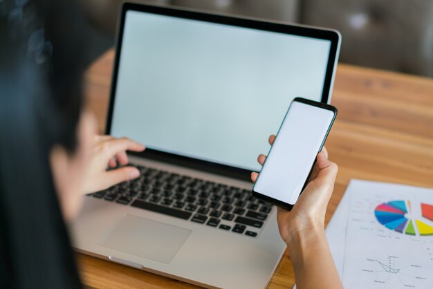 Business woman hand with Financial charts and mobile phone over laptop on the table .