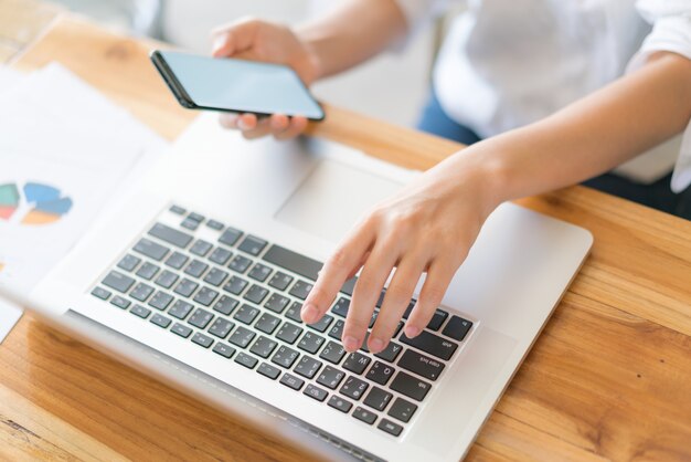 Business woman hand with Financial charts and mobile phone over laptop on the table .