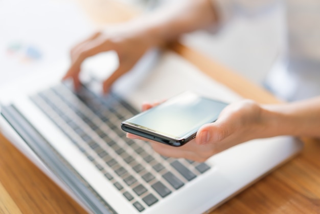 Business woman hand with Financial charts and mobile phone over laptop on the table .