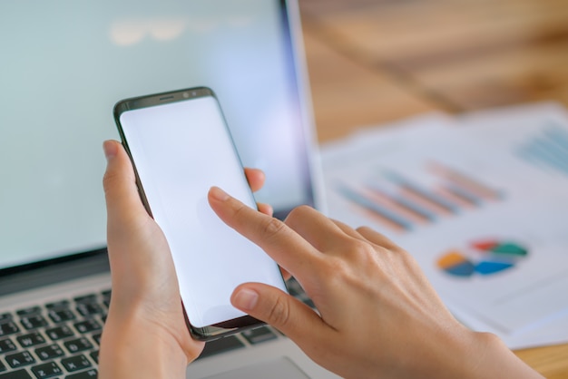 Business woman hand with Financial charts and mobile phone over laptop on the table .