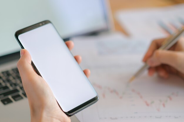 Business woman hand with Financial charts and mobile phone over laptop on the table .