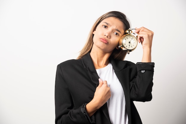 Business woman holding an alarm clock on white wall. 