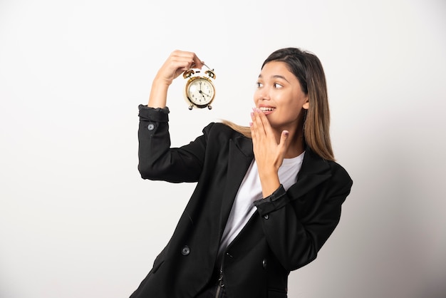 Business woman looking on an alarm clock on white wall. 