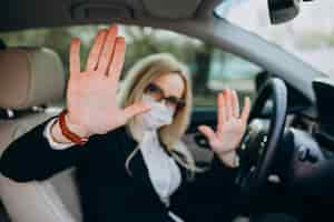 Free photo business woman in protection mask sitting inside a car using antiseptic