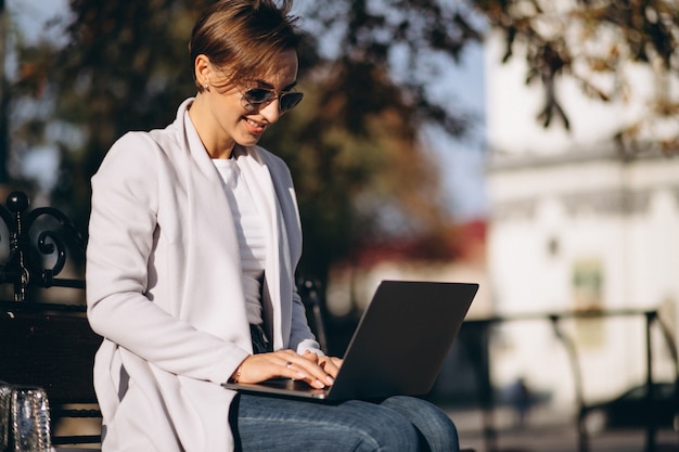 Business woman sitting on a bench in park,working on computer