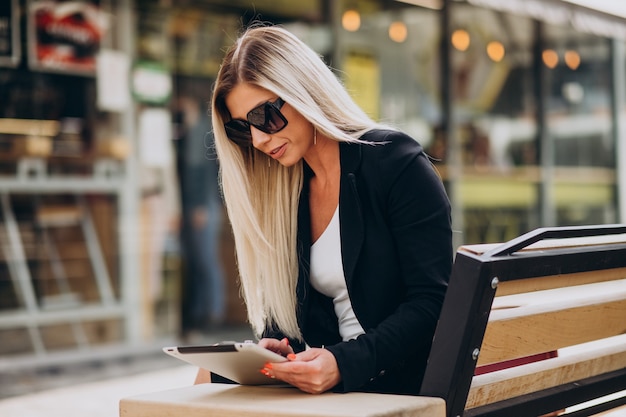 Free photo business woman sitting on bench and working on tablet