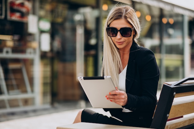 Free photo business woman sitting on bench and working on tablet