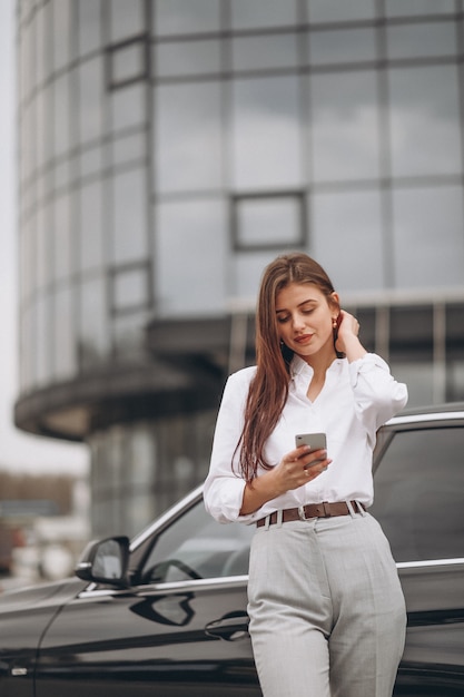 Business woman standing by the car and using phone