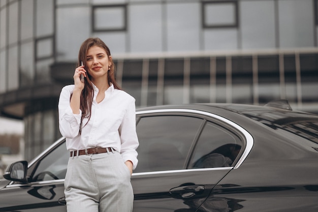 Free photo business woman standing by the car and using phone