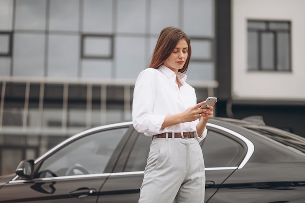 Business woman standing by the car and using phone