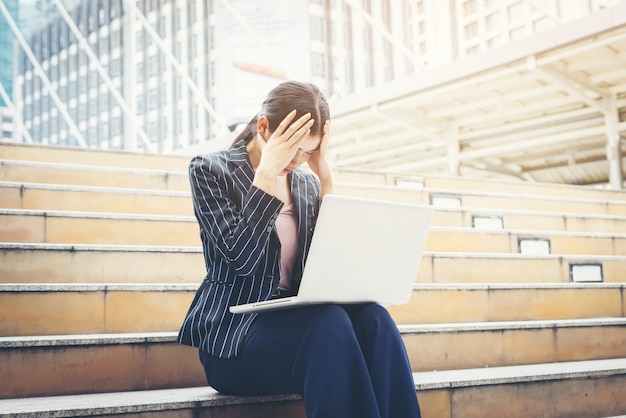 Free Photo business woman stressed while using laptop sits on the steps. business people concept.