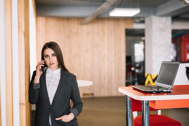 Business woman talking by phone at wall in office 