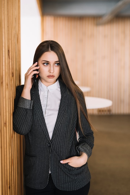 Business woman talking by phone at wall