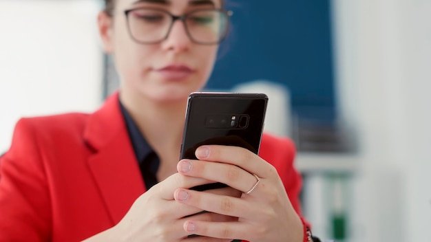 Business woman texting messages and browsing internet on smartphone, working on financial research with statistics report. Female employee using mobile phone in startup office. Close up.