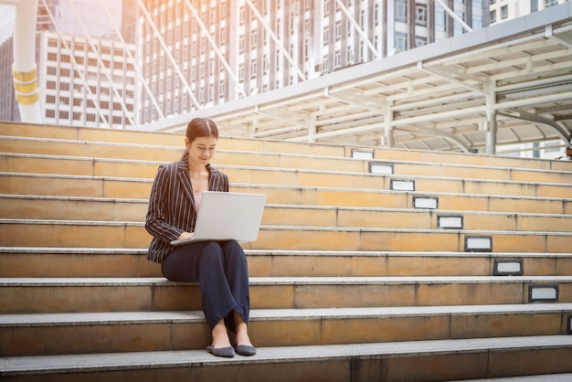 Free Photo business woman using laptop sits on the steps. business people concept.