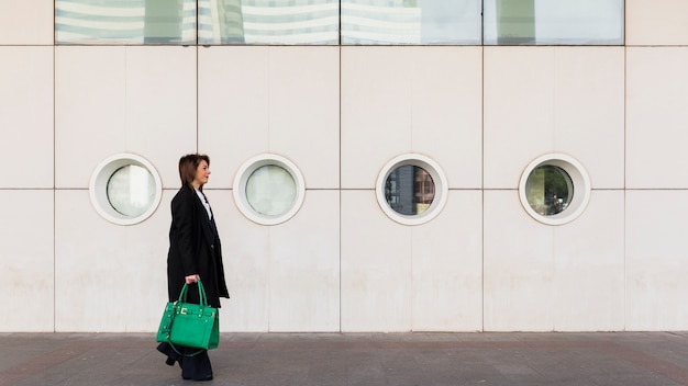 Free Photo business woman walking in street with green bag